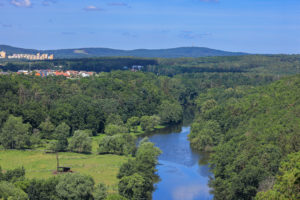 Bližší pohled proti proudu Berounky, která je vidět ve střední části snímku. Pravou část snímku tvoří výhradně lesy, do levé části zasahuje Plzeňská zástavba a vlevo v popředí louka u řeky.