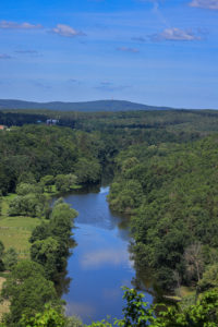 Pohled proti proudu řeky, která je vidět ve střední části snímku. Snímek tvoří téměř výhradně jen zalesněné svahy a kopce. V pozadí vrch Krkavec.