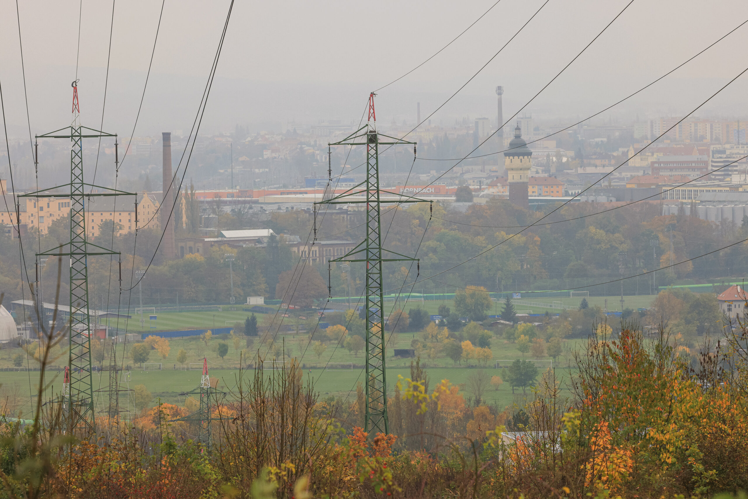 <h1>Pohled z vrchu Mikulka</h1><br />
Pohled do krajiny z vyvýšeného místa přes elektrické vedení – 2 mohutné sloupy a mnoho kabelů. Spodní polovinu tvoří převážně travnaté plochy, zadní starší průmyslová zástavba a další městská výstavba mizející v mlze.