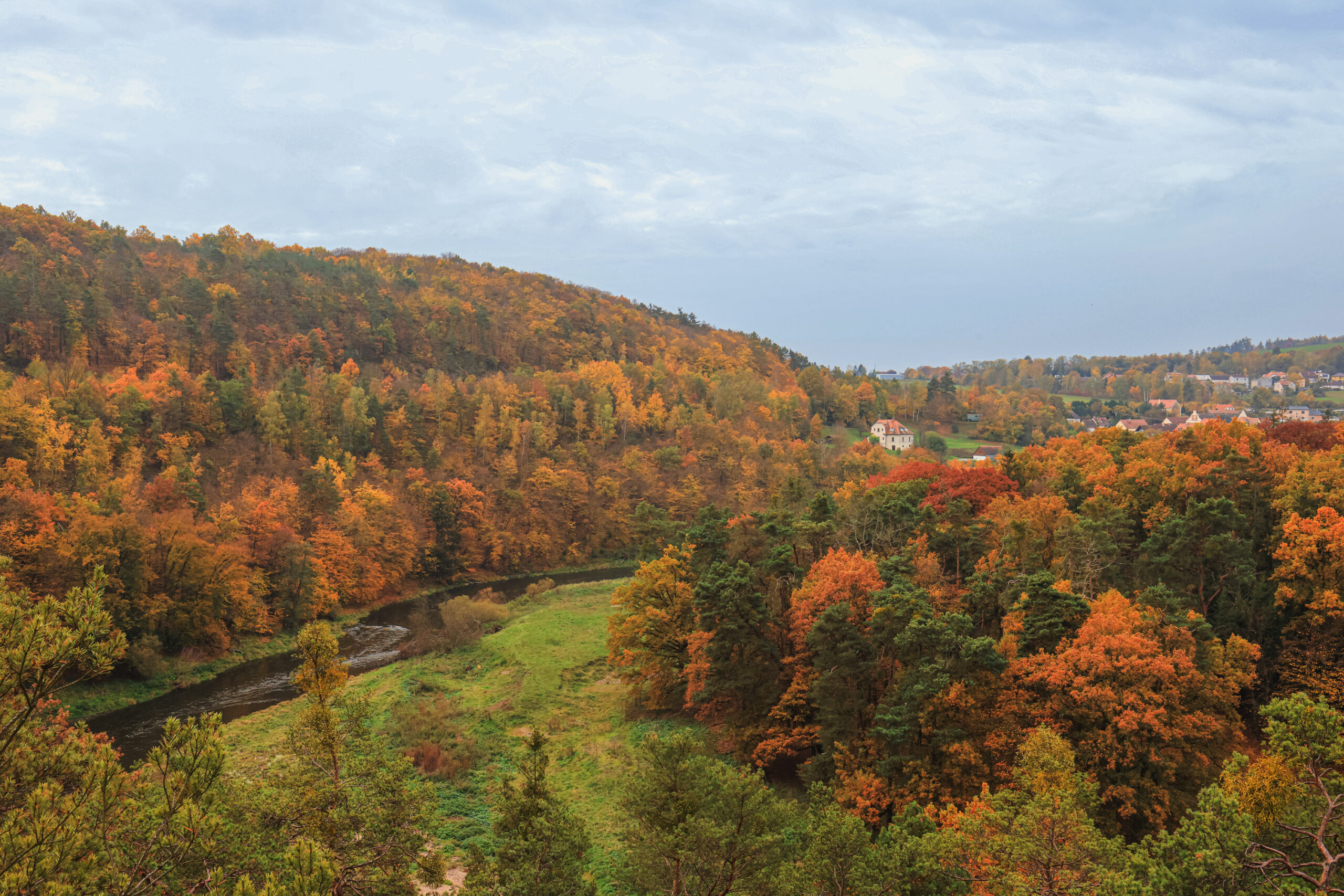 <h1>Zábělá – pohled z vyhlídky Kozí Bouda</h1><br />
Po obou stranách prochází zalesněné svahy lemující břehy Berounky. V pozadí vpravo zástavba Bukovce. Podzimní scenérie, listnaté stromy v nejrůznějších barvách – odstíny zelené, žluté, červené, oranžové, hnědé.