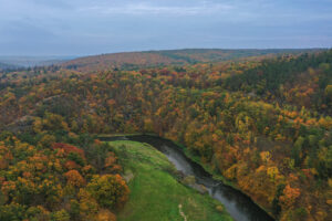 Pohled na Zábělou z ptačí perspektivy. V popředí prochází Berounka stáčející se k levé straně snímku. Podzimní scenérie – stromy v nejrůznějších odstínech.