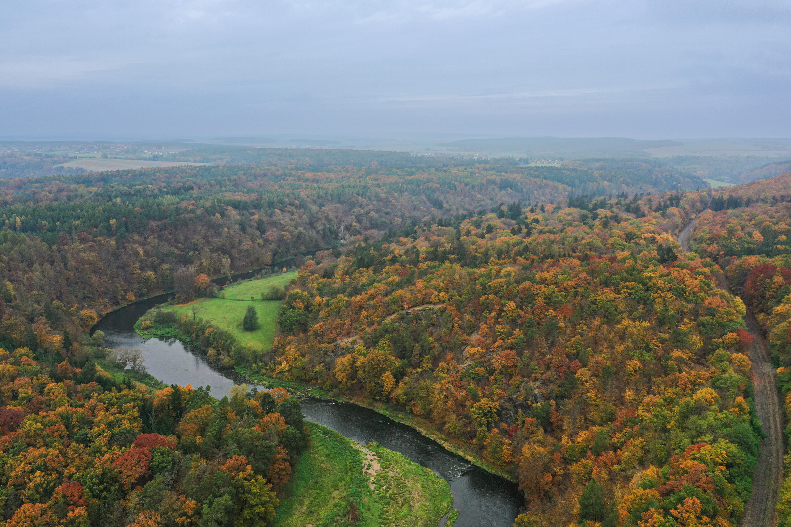 <h1>Zábělá a Háj</h1><br />
Podzimní krajina z ptačí perspektivy. Na pravé a střední části snímku Zábělá. Podél levého okraje viditelný koridor bývalé železnice. V levé a zadní části lokalita Háj – souvislý lesní porost. Středem se vine řeka. Stromy v nejrůznějších odstínech.